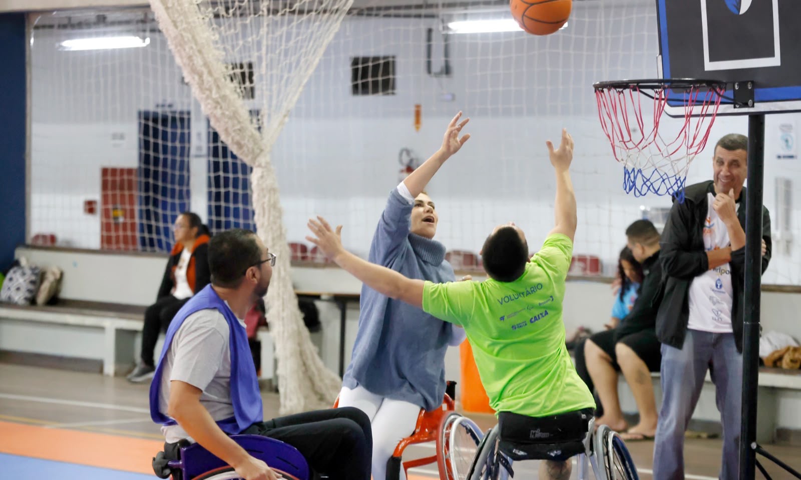 Participante arremessa a bola durante atividade de basquetebol em cadeira de rodas