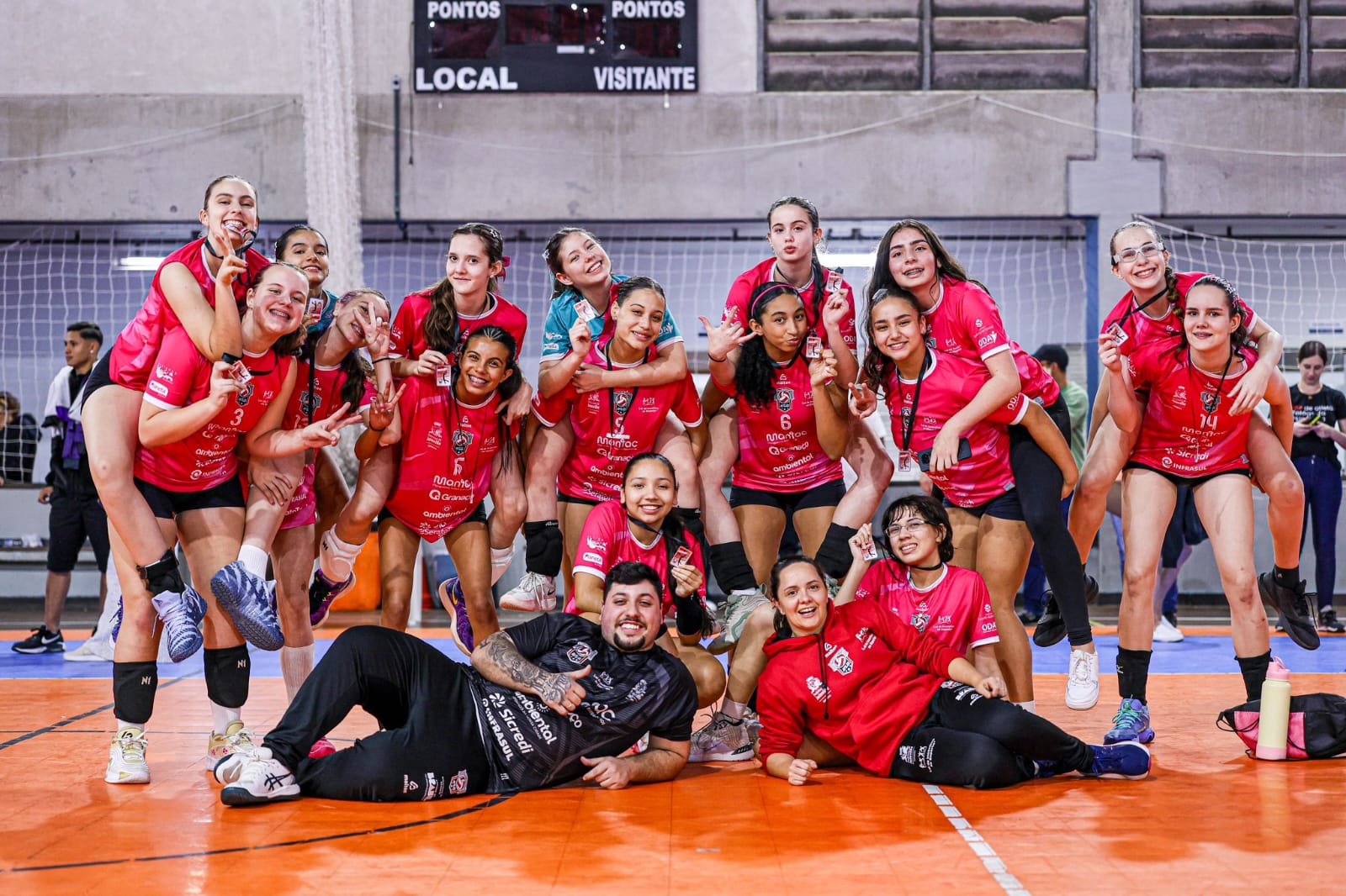 Equipe feminina de voleibol reunida em quadra com medalhas
