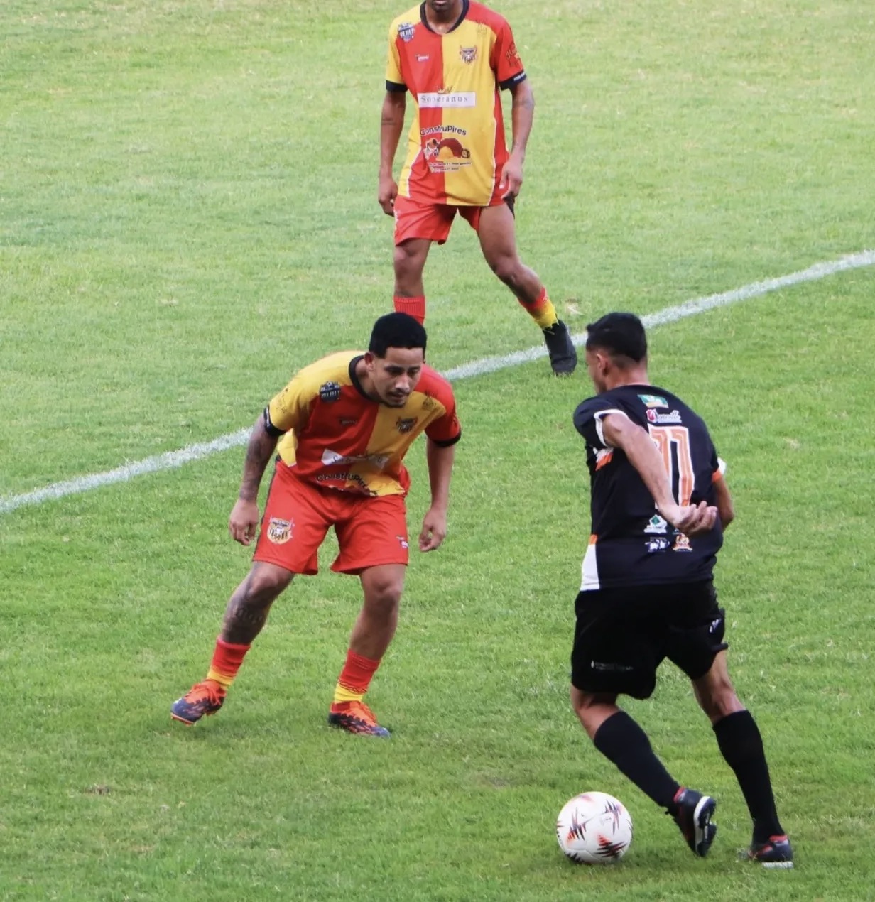 Jogadores de uniformes vermelho e amarelo e preto em lance de futebol