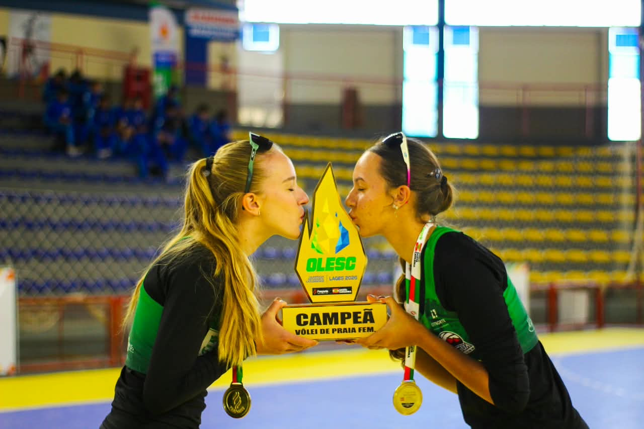 Duas atletas com medalhas beijam o troféu de campeã do vôlei de praia feminino da Olesc de 2026, em Lages.